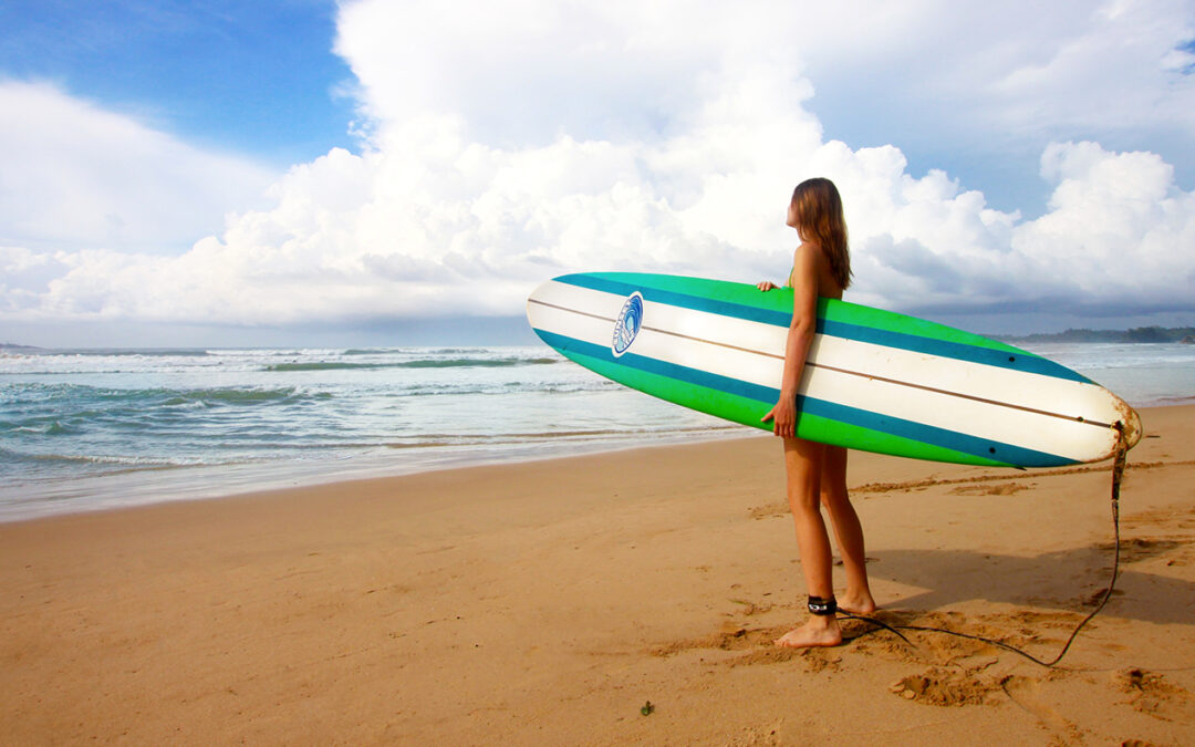femme surfeuse admirant l'océan depuis la plage sa planche de surf sous la main, le cycle menstruel féminin est comparable à une vague de surf