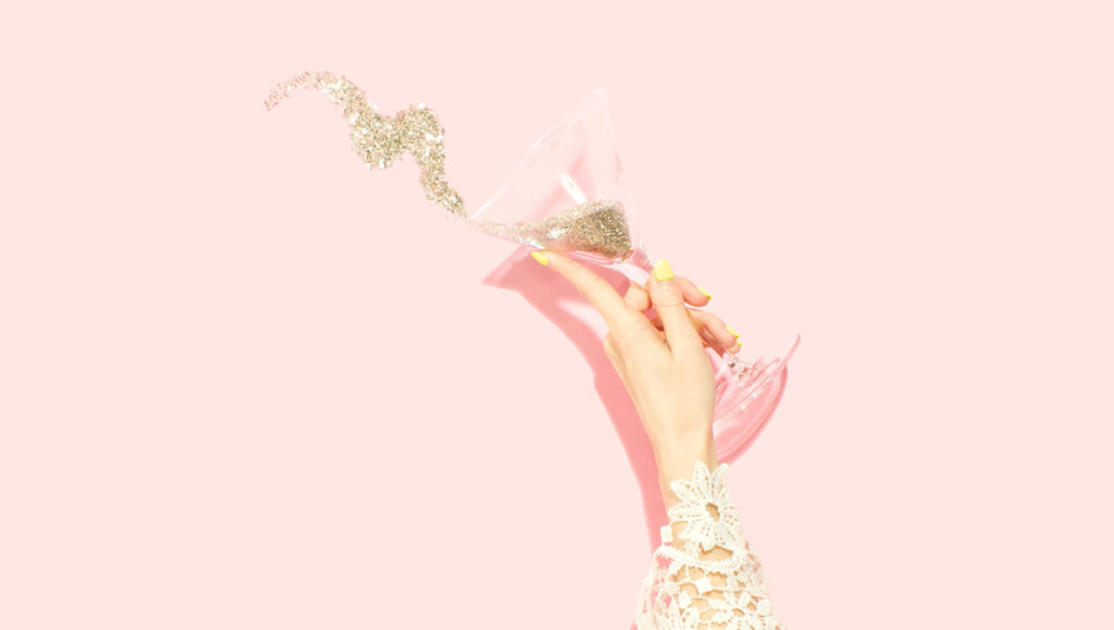 main de femme tenant une coupe remplie de paillettes dorées sur fond rose durant la deuxième semaine après ses règles