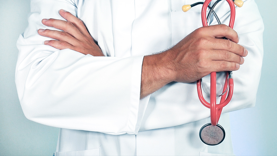 Un médecin les bras croisés tenant un stéthoscope rouge à la main droite, en cas d’œdème ou de gonflement persistants une consultation médicale et idéale.